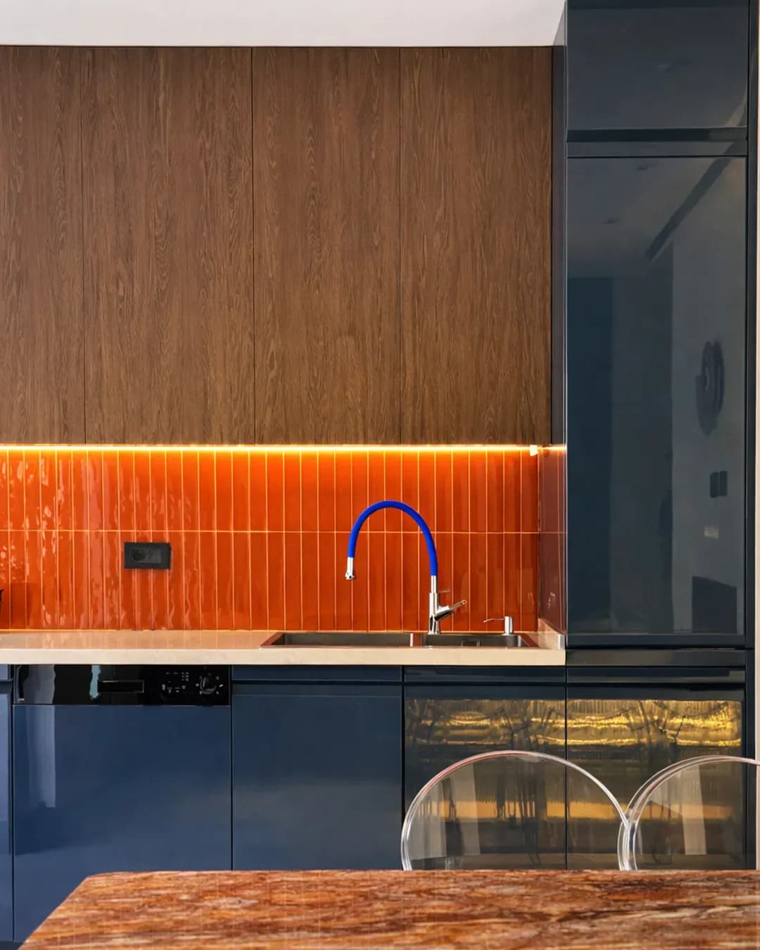 Cuisine Cuisina contemporaine avec façades bleu nuit, crédence orange brillante, éléments en bois et rangements intégrés.